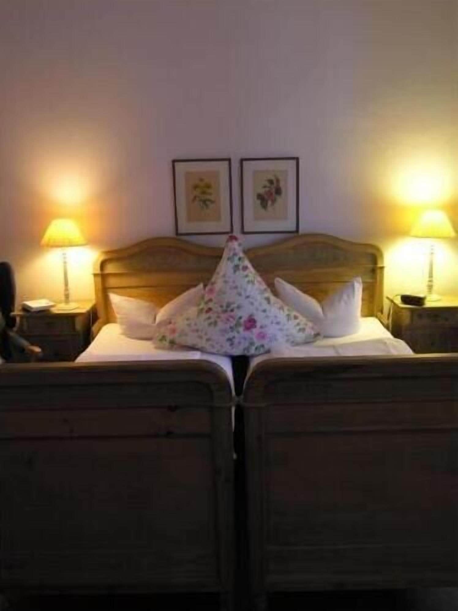 A double bed with floral bedding, two bedside lamps, and two framed pictures on the wall.