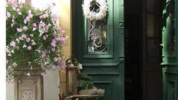 Una puerta verde con un adorno de corona, una planta en maceta y una pequeña mesa con una silla frente a un edificio.