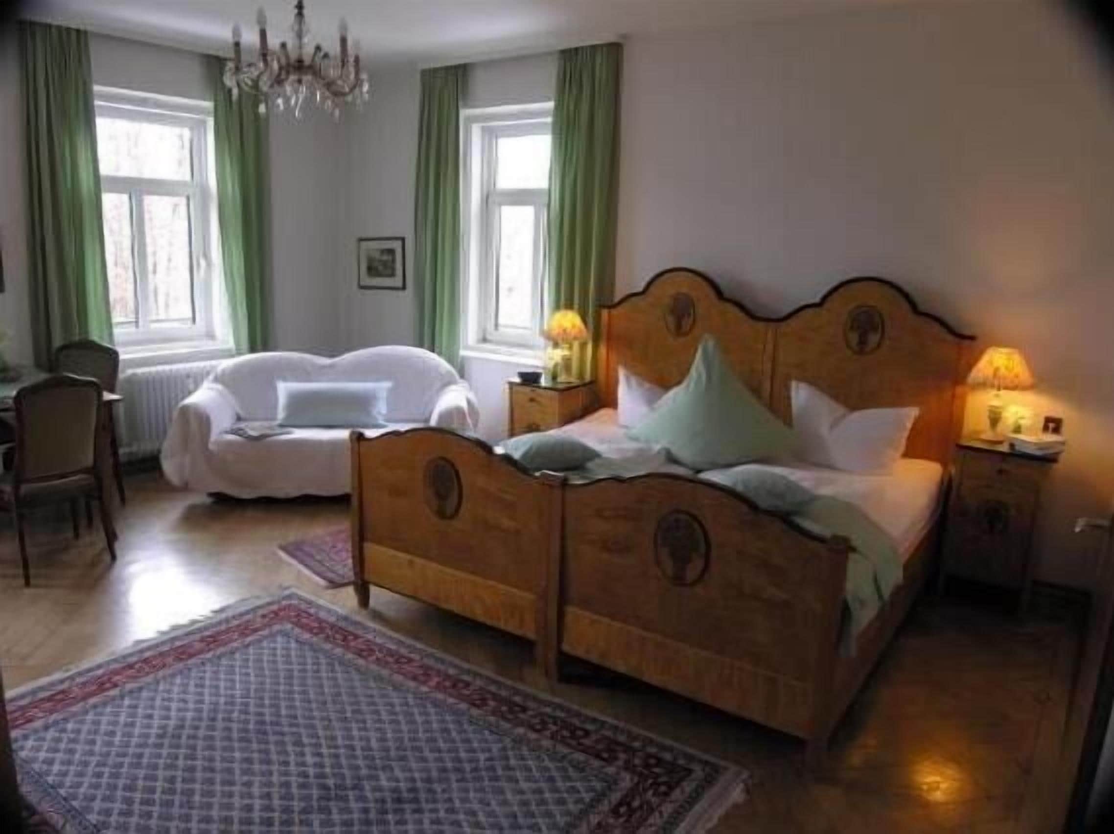 Ein Schlafzimmer mit einem hölzernen Bett, grünen Vorhängen, einer Chandelier und einem Sessel.