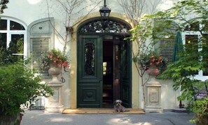 A historic building with a green ornate entrance, a small dog sitting outside, and classical architecture. - Hotel Kolbergarten (Bad Toelz)