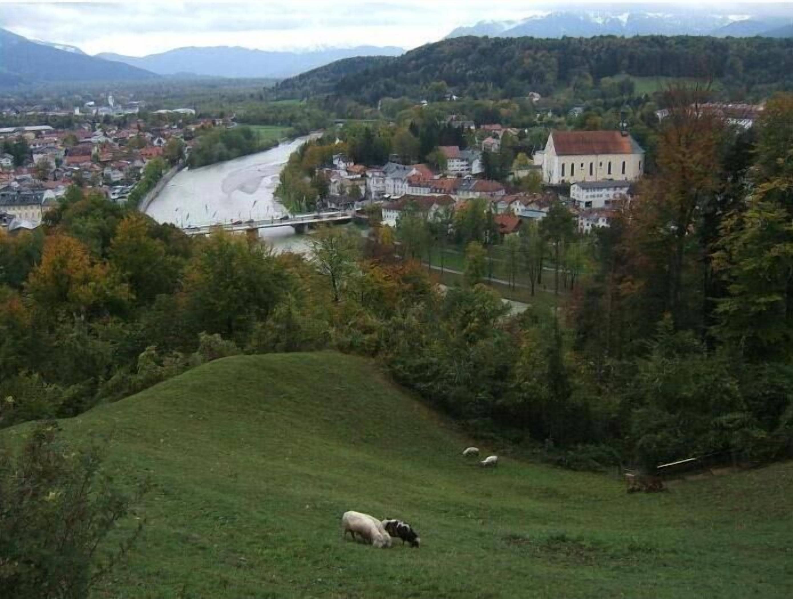 Un paysage rural avec une rivière, un pont et une colline où paissent des moutons.