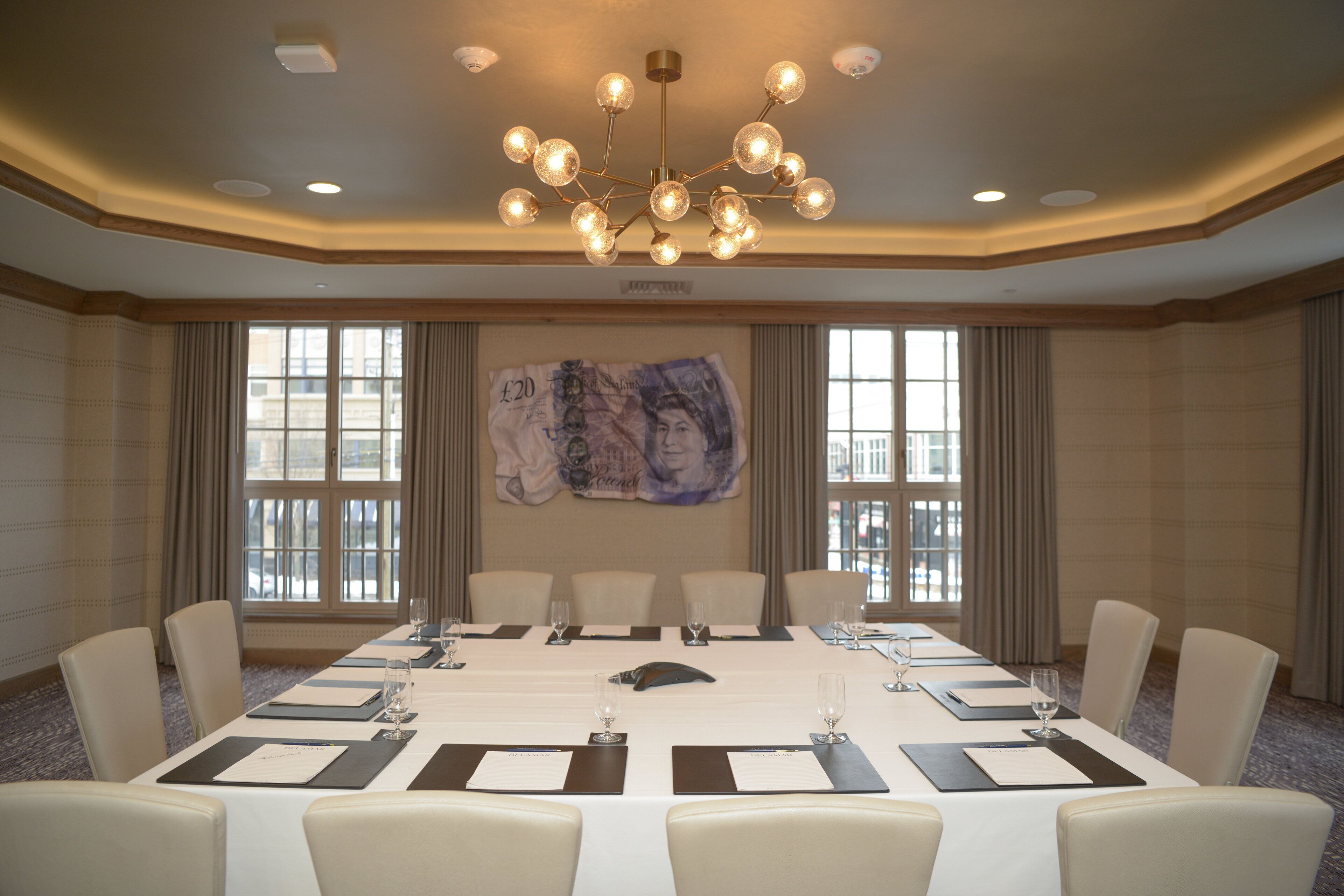 A conference room with a long table, multiple chairs, a chandelier, and large windows with curtains.
