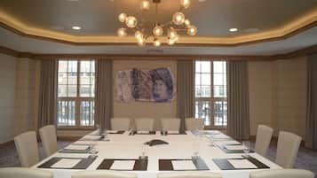 A conference room with a long table, multiple chairs, a chandelier, and large windows with curtains.
