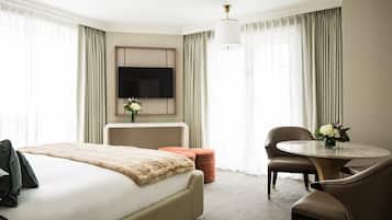 Ein Hotelzimmer mit Bett, Schreibtisch, Stuhl, rundem Tisch, Fernseher und einer Vase mit Blumen.