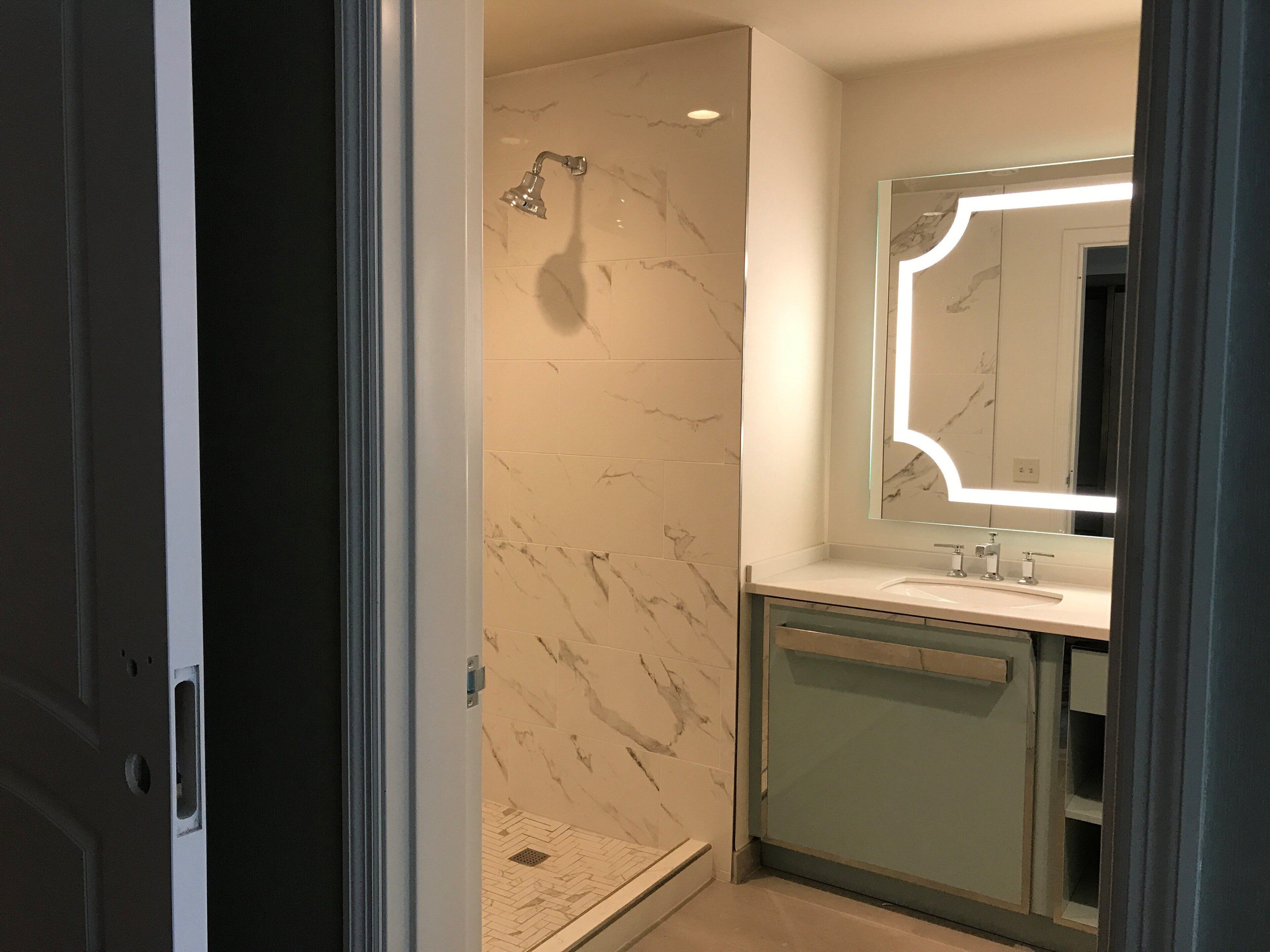 A modern bathroom with a shower, a vanity with a mirror, and a marble backsplash.