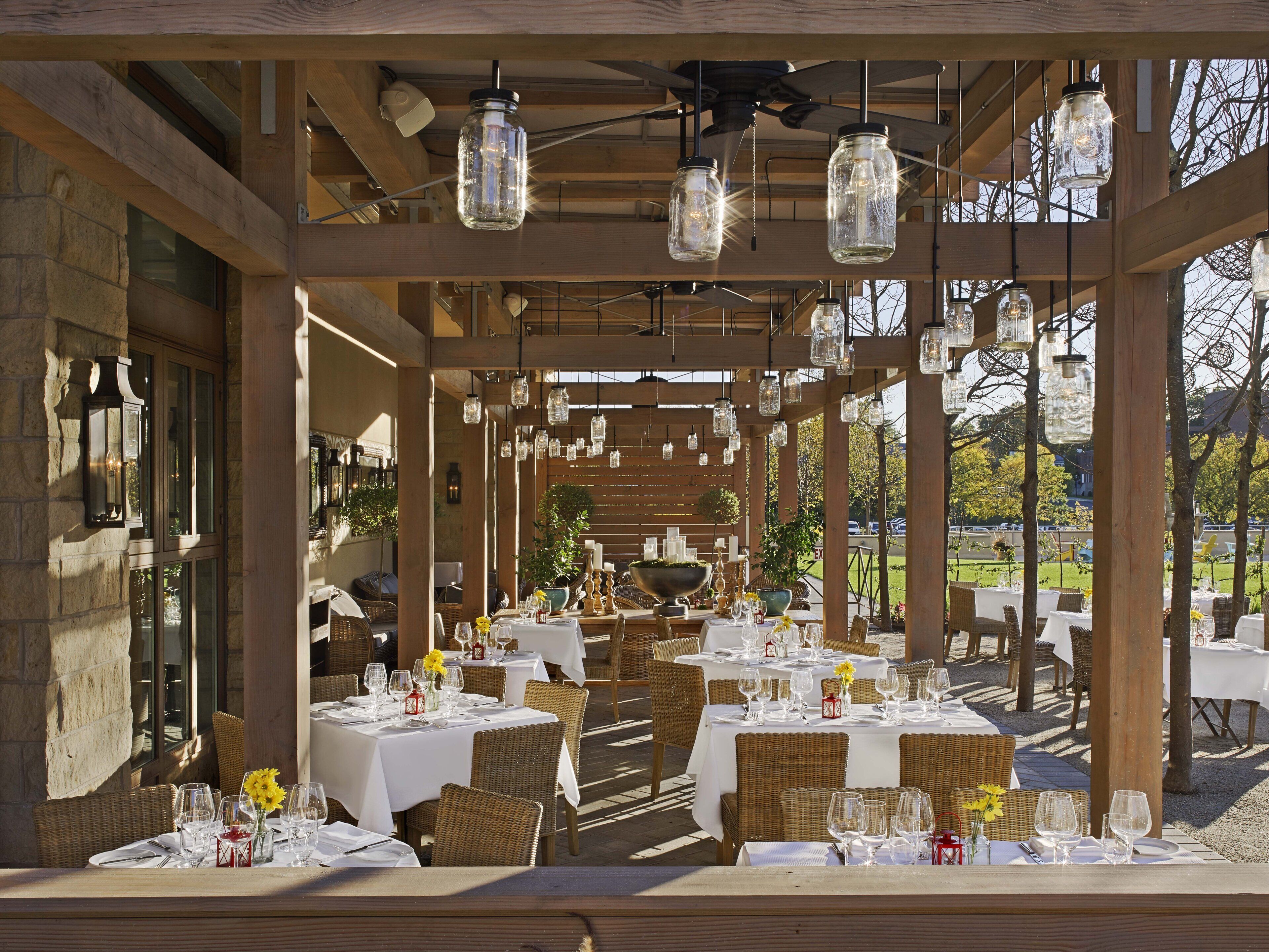 Un espace de restauration en plein air avec des tables pour deux personnes, des poutres en bois et des luminaires suspendus.