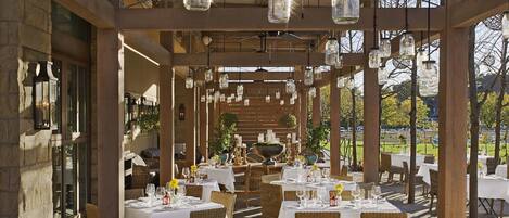 Un espace de restauration en plein air avec des tables pour deux personnes, des poutres en bois et des luminaires suspendus.