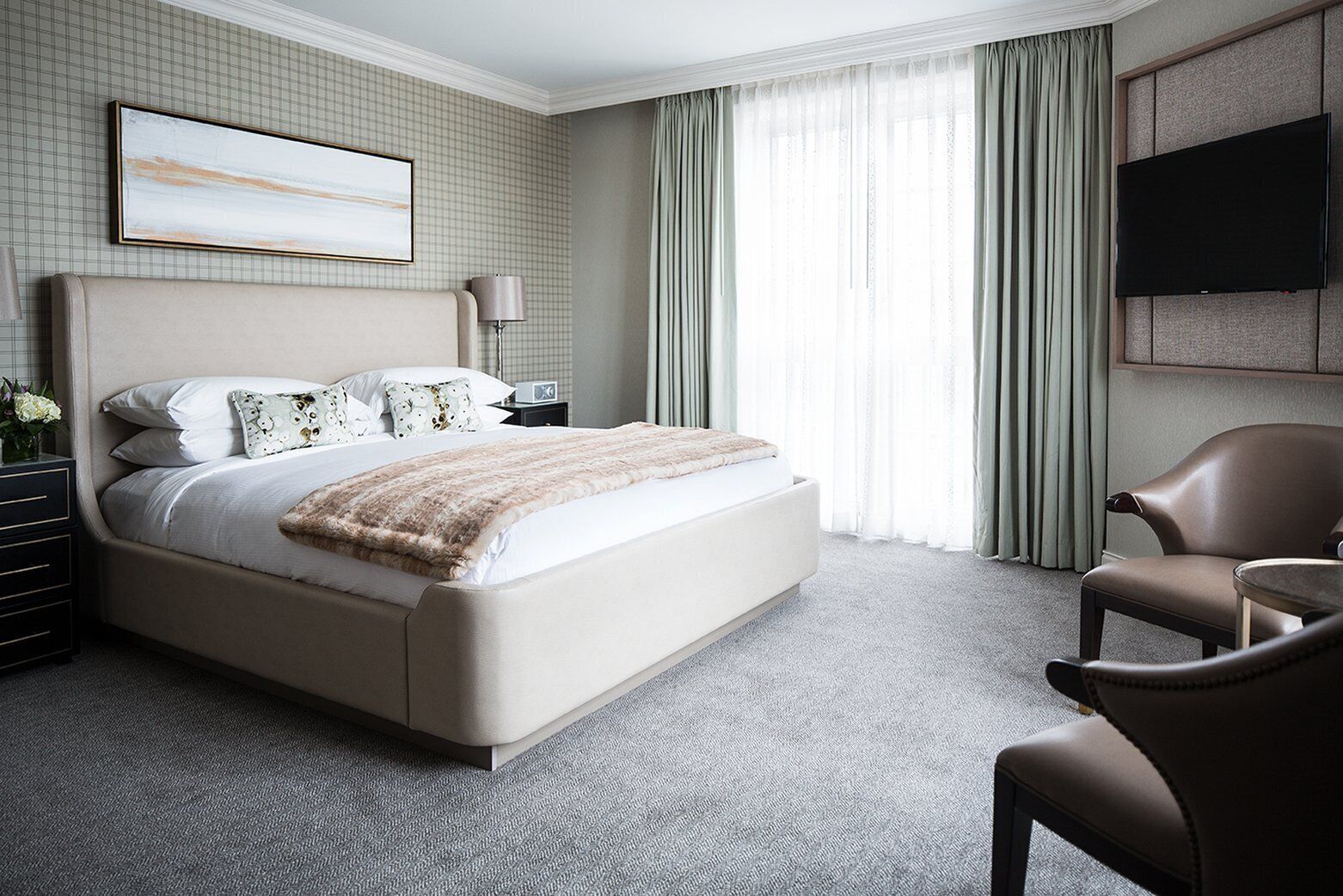 Une chambre d’hôtel avec un grand lit, un bureau, une chaise, une télévision et une fenêtre avec des rideaux.