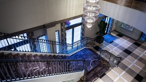 Un interior de varios niveles con una imponente escalera, un candelabro y un suelo a cuadros.
