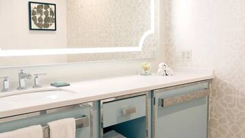 Un baño moderno con un lavamanos blanco, dos grifos, un espejo y un papel tapiz estampado.