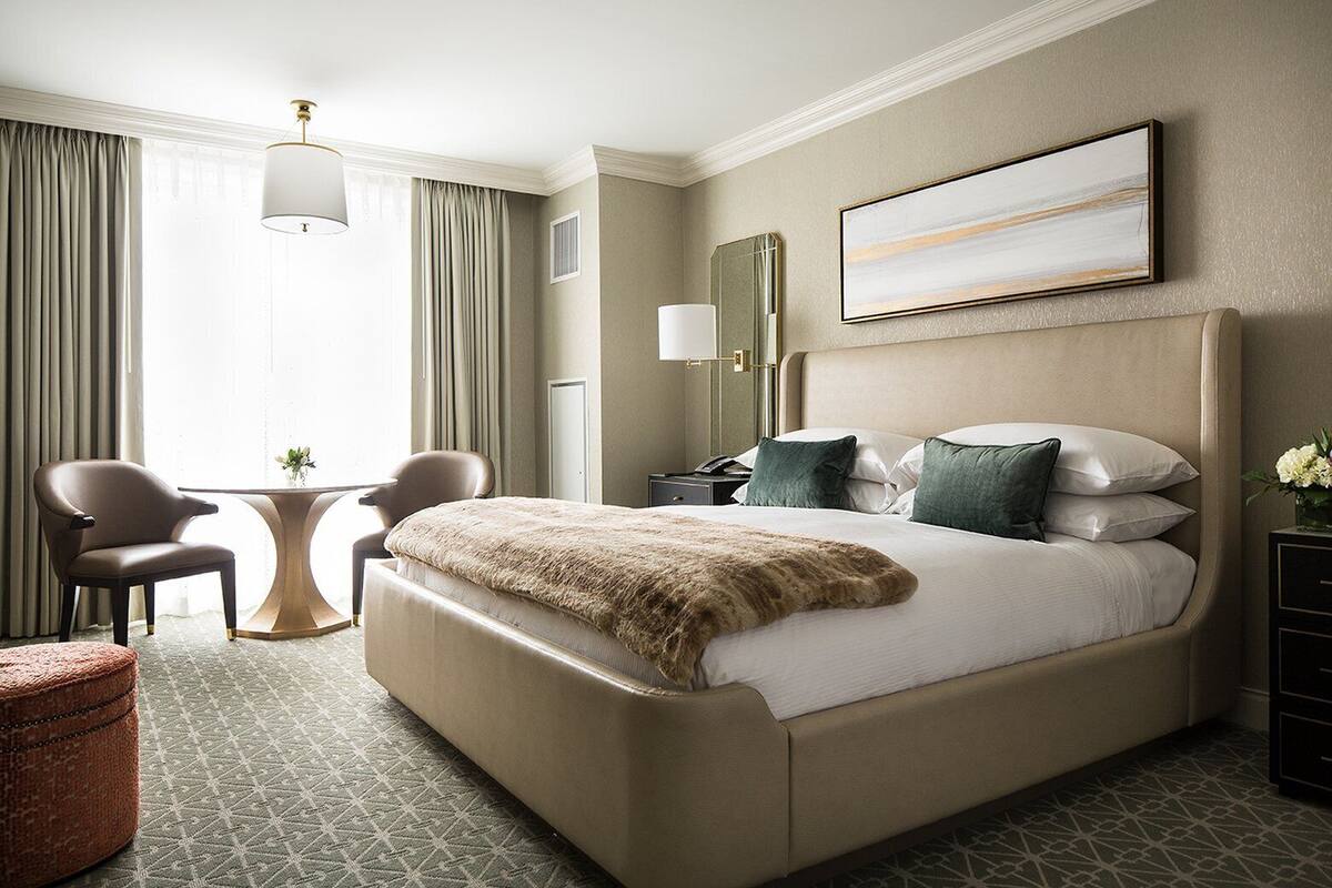 A hotel room with a large bed, two chairs, a small table, and a decorative mirror.