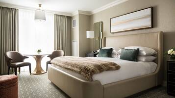 A hotel room with a large bed, two chairs, a small table, and a decorative mirror.