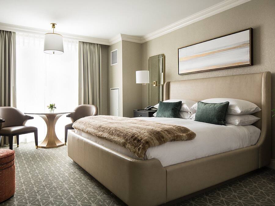 A hotel room with a large bed, two chairs, a small table, and a decorative mirror.