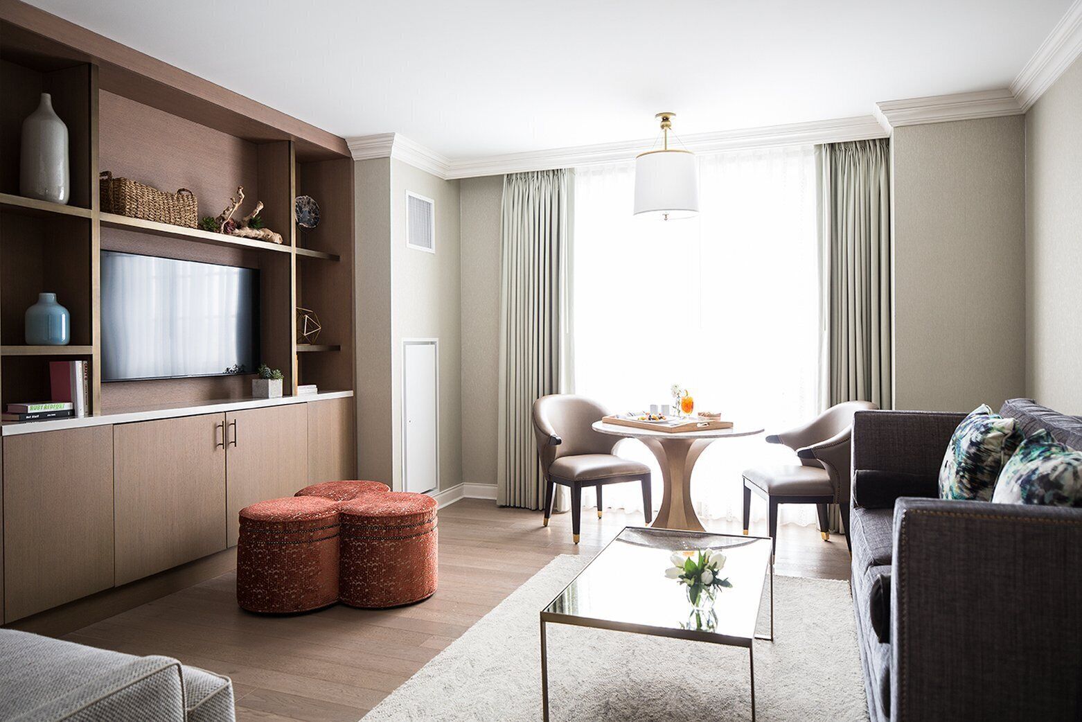 Una sala de estar moderna con un televisor de pantalla plana, una mesa redonda, dos sillones, un sofá y una estantería.