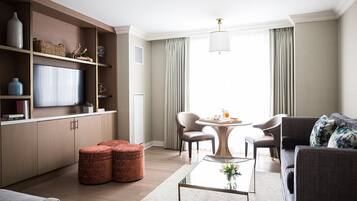 Una sala de estar moderna con un televisor de pantalla plana, una mesa redonda, dos sillones, un sofá y una estantería.