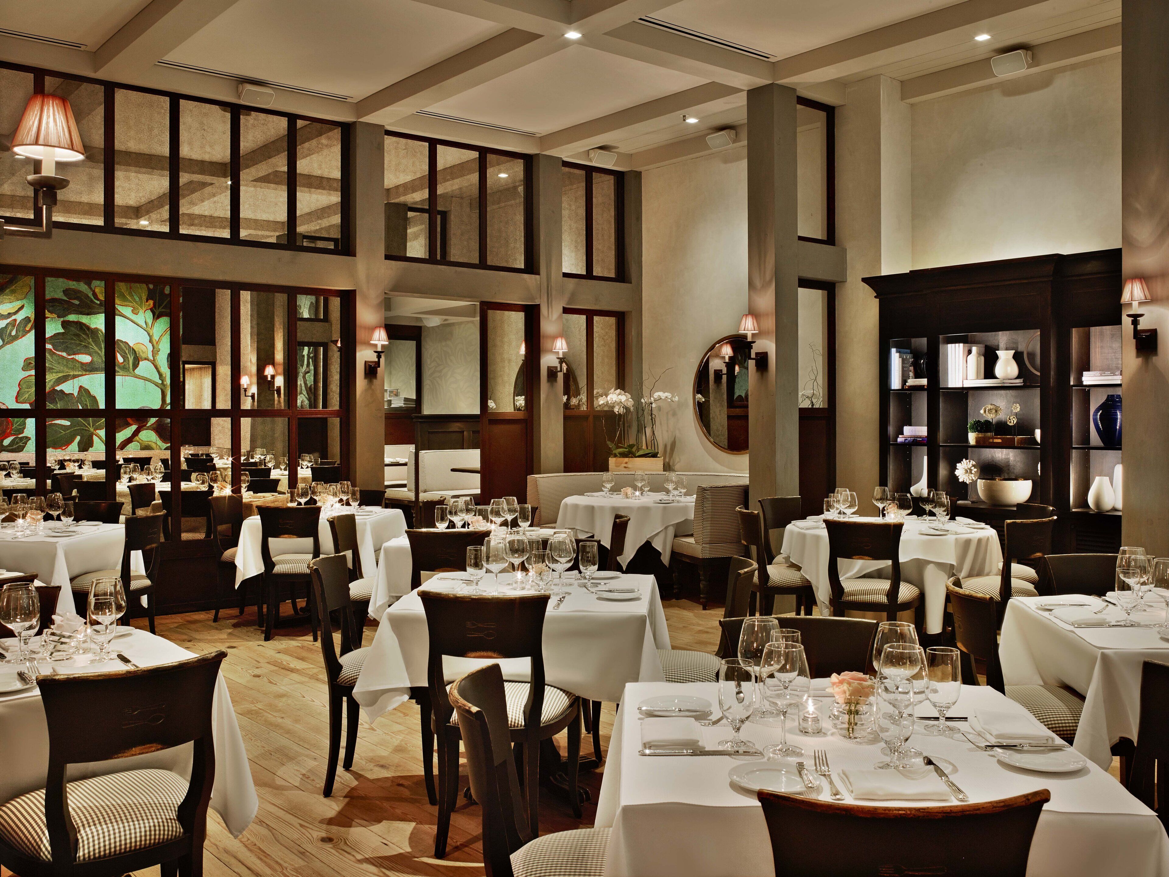 A spacious dining area with multiple tables set for dining, featuring a high ceiling and large windows.