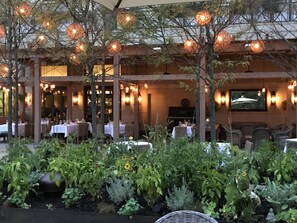 An outdoor dining area with tables and chairs, surrounded by plants and trees.