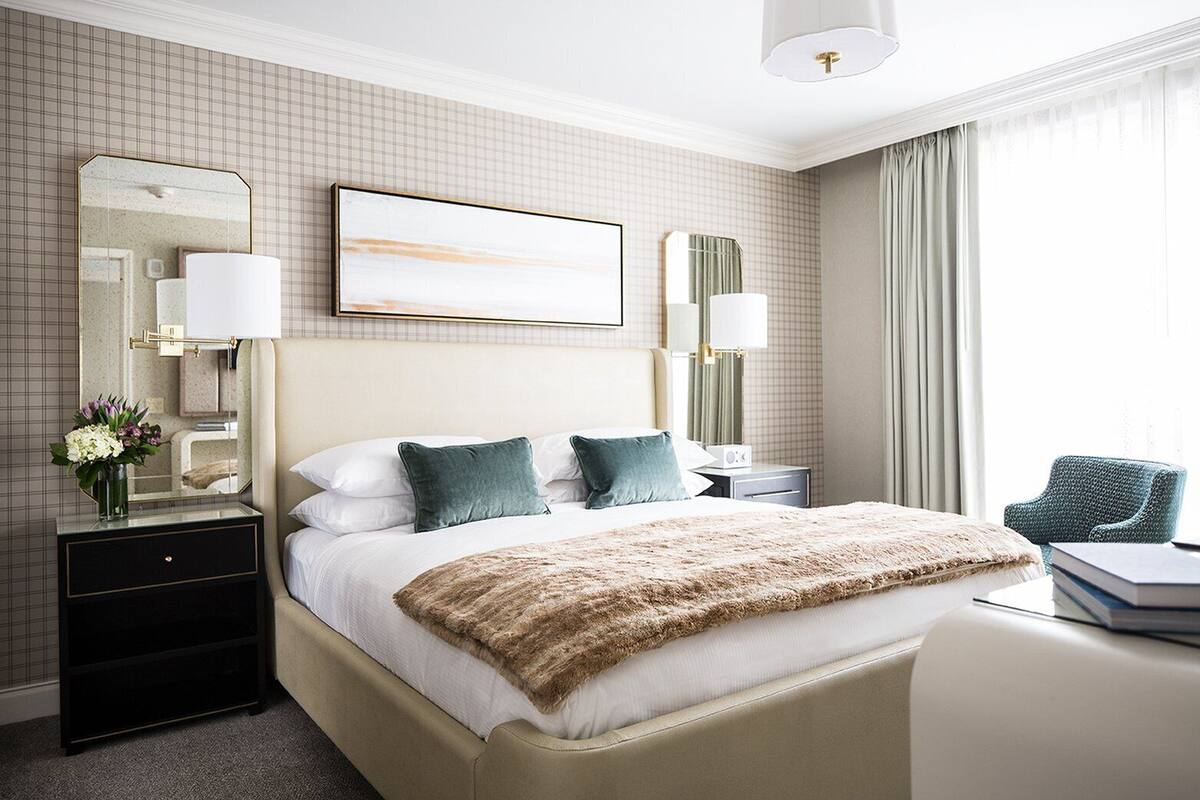 A hotel room with a large bed, two bedside tables, a mirror, and a view of the outdoors.