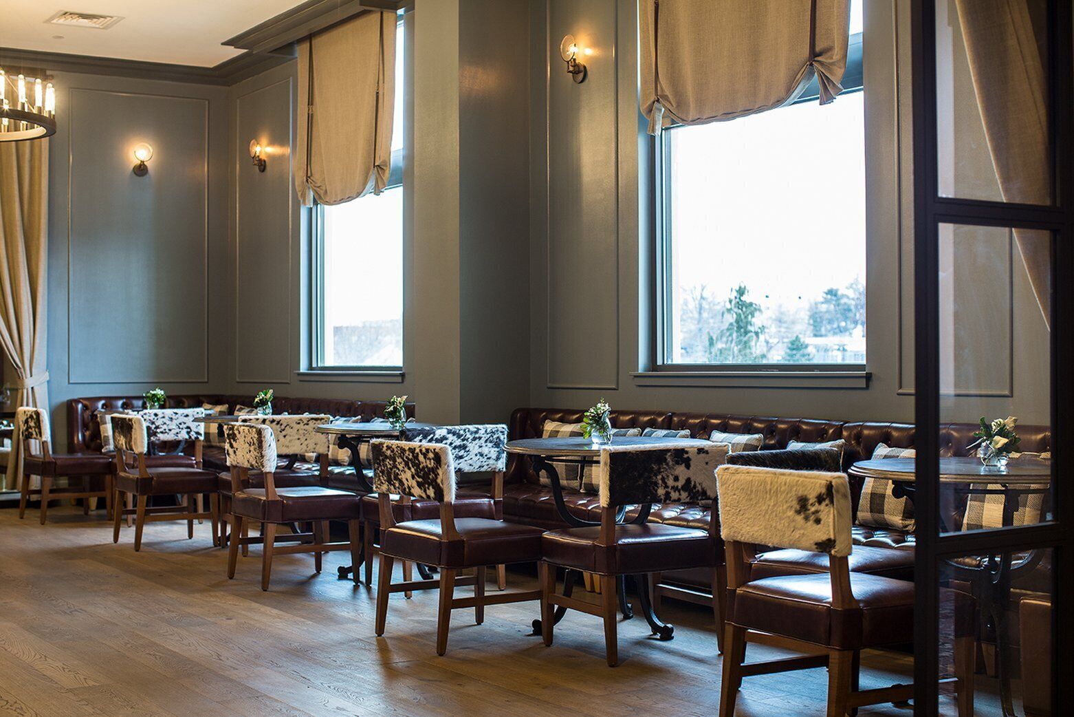 Un restaurante con mesas y sillas de madera, ventanas amplias y un candelabro.