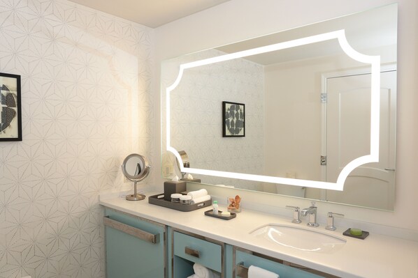 A bathroom with a large mirror, a sink, and a vanity with drawers.