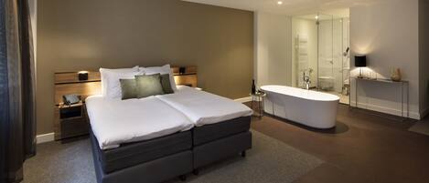 A modern hotel room with a large bed, a separate bathroom, and a walk-in shower.