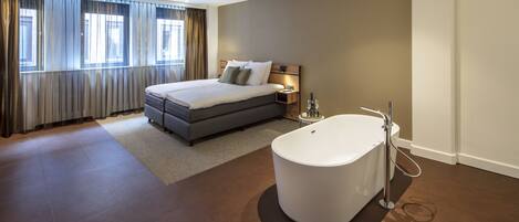 Ein modernes Hotelzimmer mit einem großen Bett, einer separaten Sitzecke, einer Badewanne und Blick auf die Stadt.