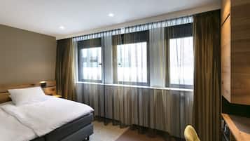 A modern hotel room with a large bed, a wooden headboard, a desk, and a chair.