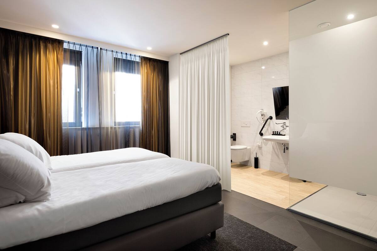 A modern hotel room with a large bed, a bathroom with a sink and mirror, and a view of the city.