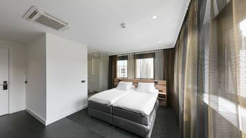 A modern hotel room with a large bed, a bedside table, a mirror, and a window with curtains.
