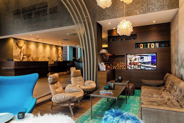 A modern hotel lobby with leather sofas, a blue armchair, a coffee table, and a TV screen displaying a cityscape. - Motel One Manchester-Royal Exchange (Manchester)