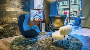 A modern lobby with a stone wall, a fireplace, blue chairs, and a large window with a view of the street.