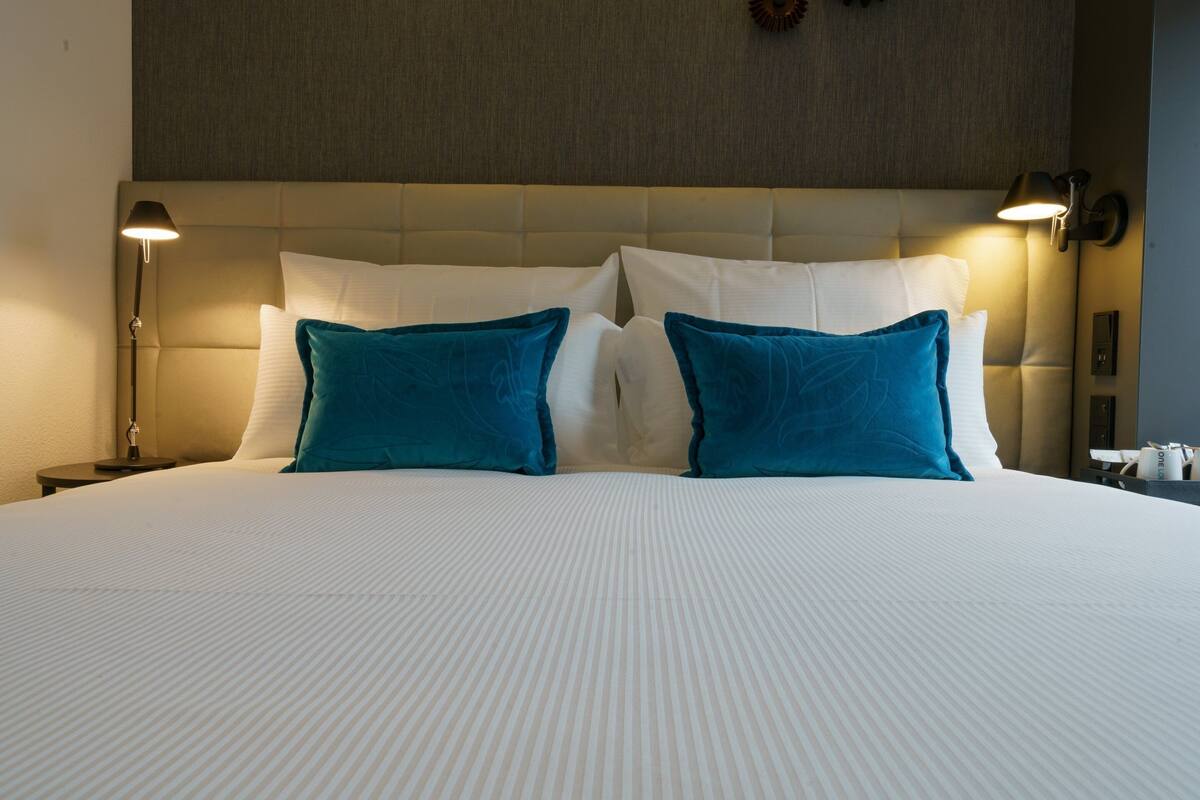 A neatly made bed with white and teal pillows, a tufted headboard, and a bedside lamp.