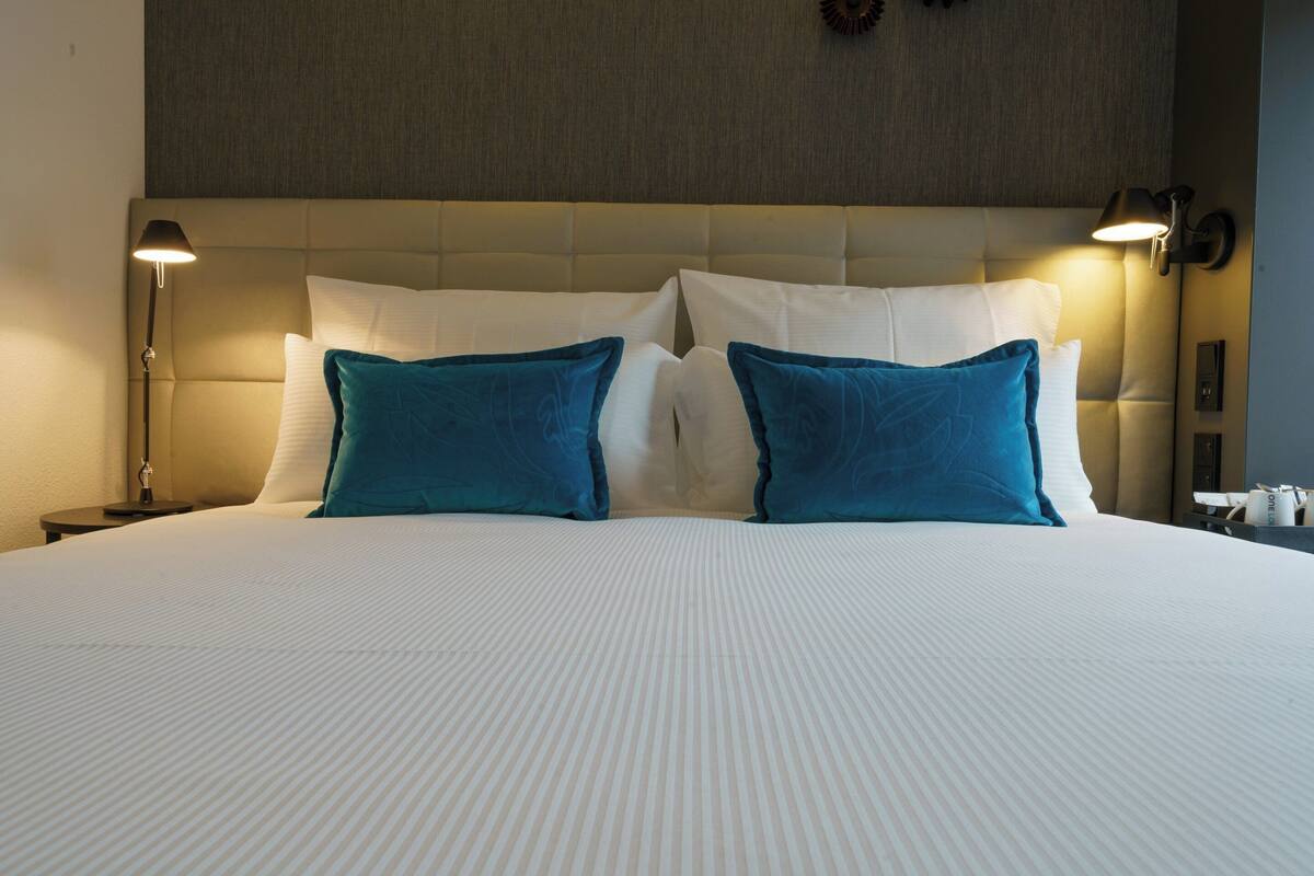 A neatly made bed with white and teal pillows, a tufted headboard, and a bedside lamp.
