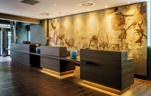 A reception area with a modern design, featuring a reception desk, a large decorative wall, and a wooden floor. - Motel One Manchester-Royal Exchange (Manchester)