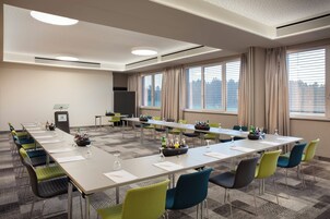 Un salón de conferencias con una larga mesa, varias sillas y un atril.