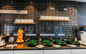 Un buffet avec une pancarte indiquant « PROFITEZ DE LA NOURRITURE ET DES BOISSONS » et une pile d’oranges.