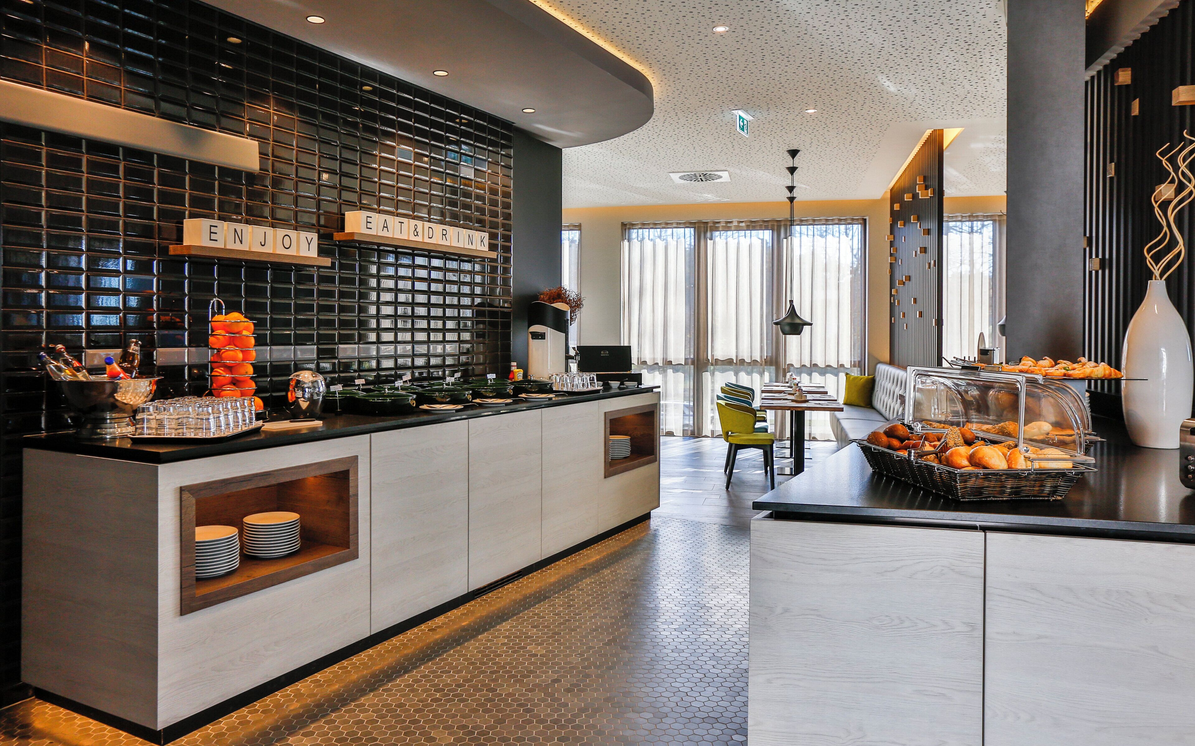 Eine moderne Hotelhalle mit einer Rezeption, einer Sitzecke und einem Frühstücksbuffet.