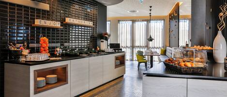 Eine moderne Hotelhalle mit einer Rezeption, einer Sitzecke und einem Frühstücksbuffet.