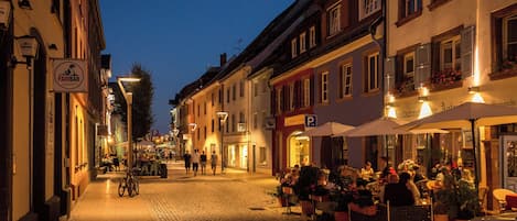 A cobblestone street lined with buildings, some with outdoor seating and umbrellas, indicating a dining area.