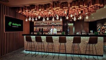 Zona de bar con techo de madera, lámparas colgantes y un camarero.