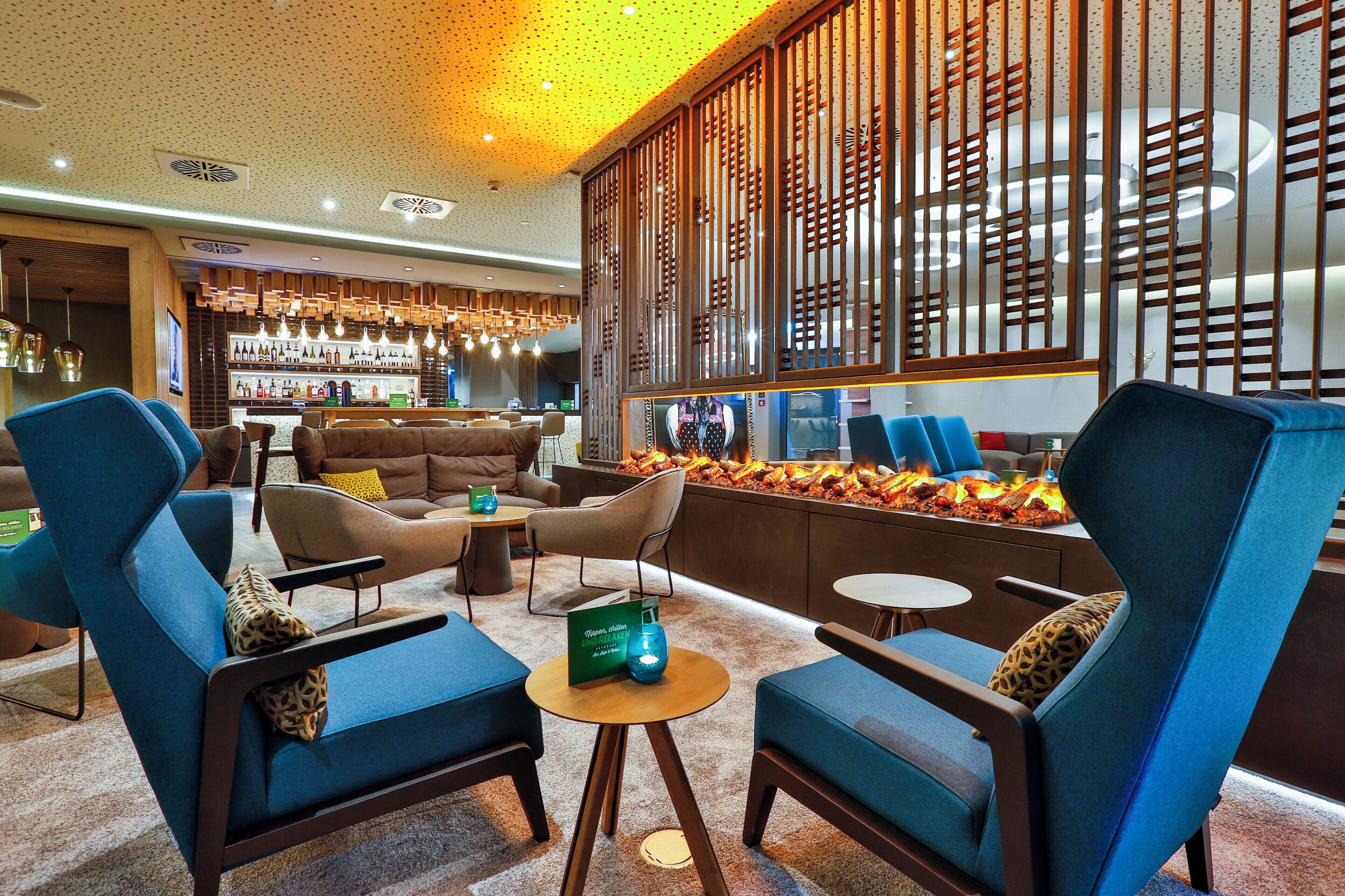 A modern lounge area with blue armchairs, a sofa, and a bar with a variety of bottles.