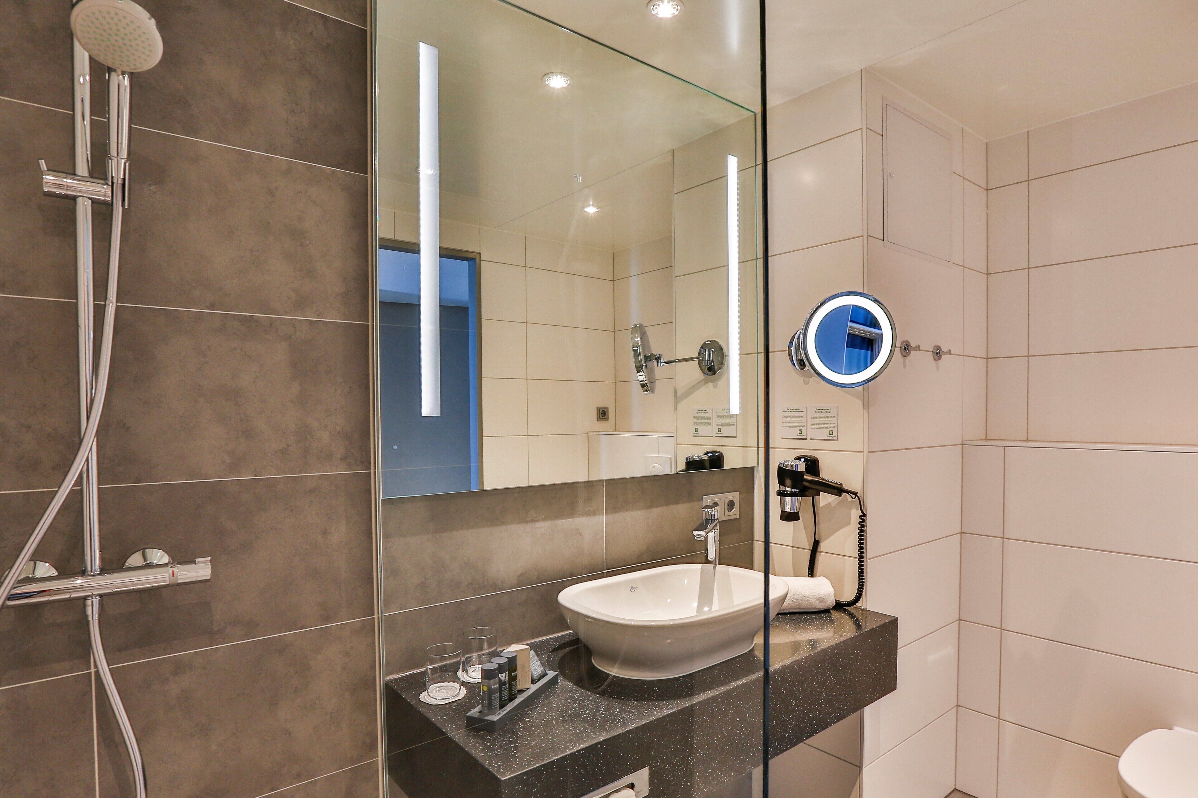 A modern bathroom with a glass shower enclosure, a white sink, and a mirror with a round inset.
