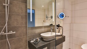 A modern bathroom with a glass shower enclosure, a white sink, and a mirror with a round inset. - Holiday Inn Villingen - Schwenningen by IHG (Villingen-Schwenningen)