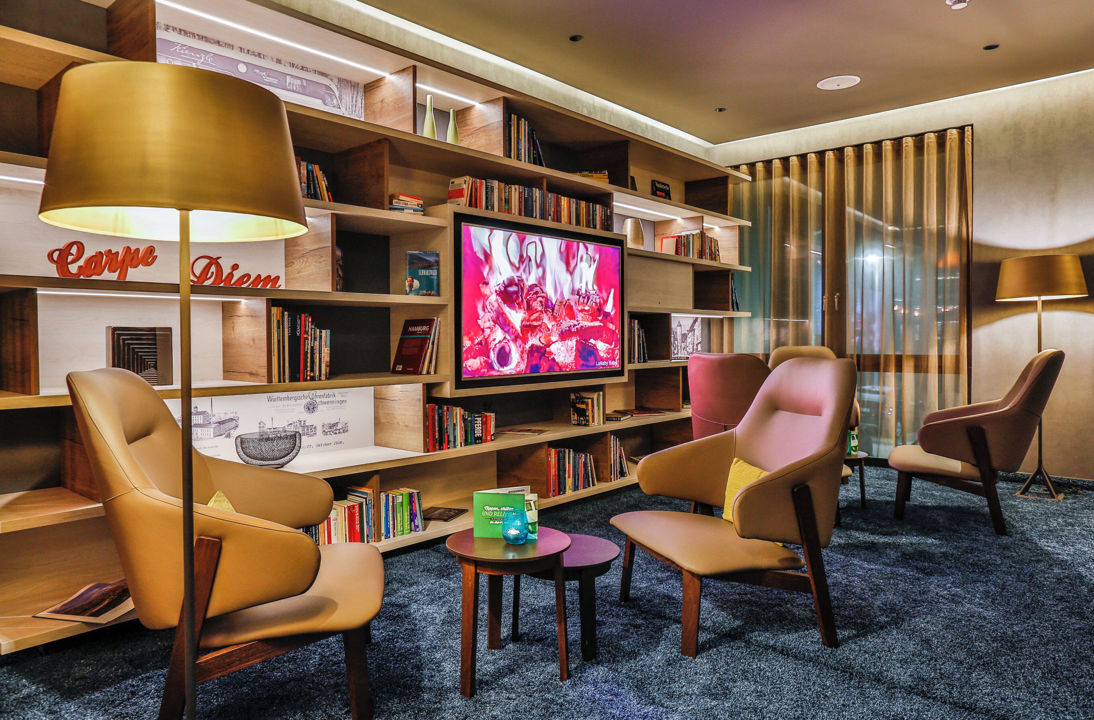 Un salón de hotel con sillones de cuero, un televisor y estanterías.