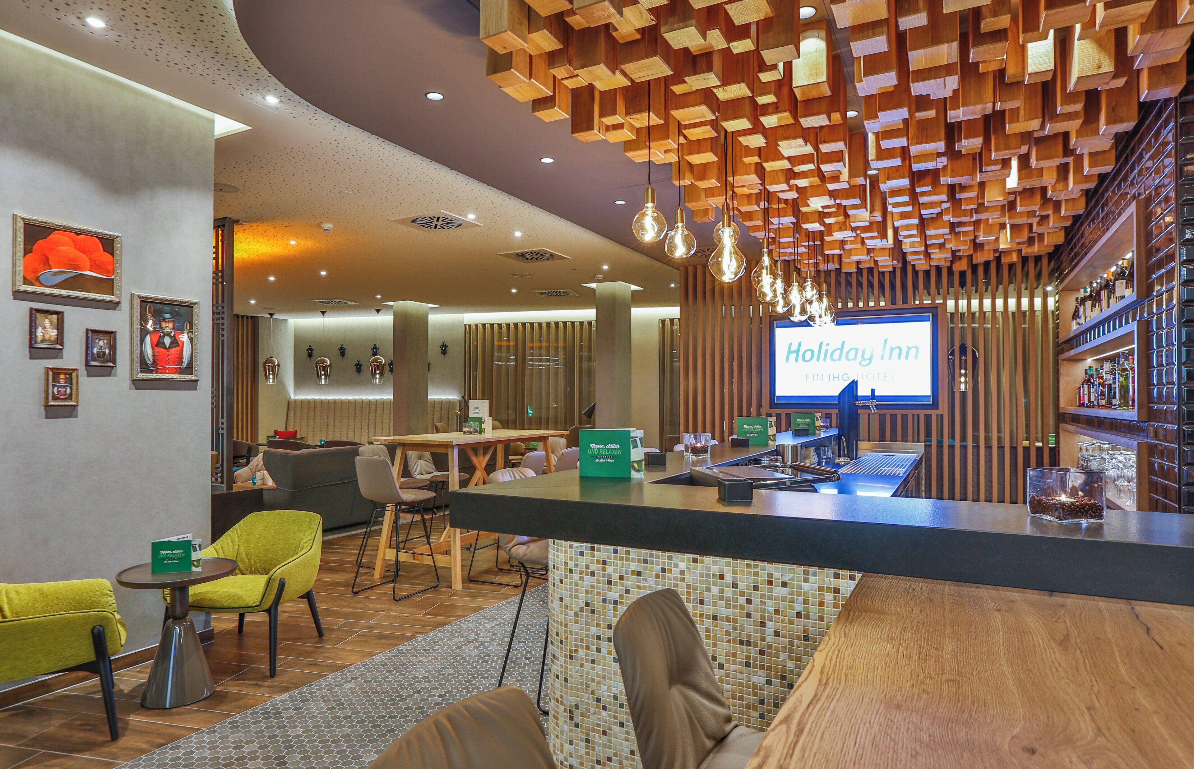 Eine Hotelhalle mit einer Rezeption, einer Sitzecke und einem an der Wand befestigten Fernseher, der 'Holiday Inn' anzeigt.