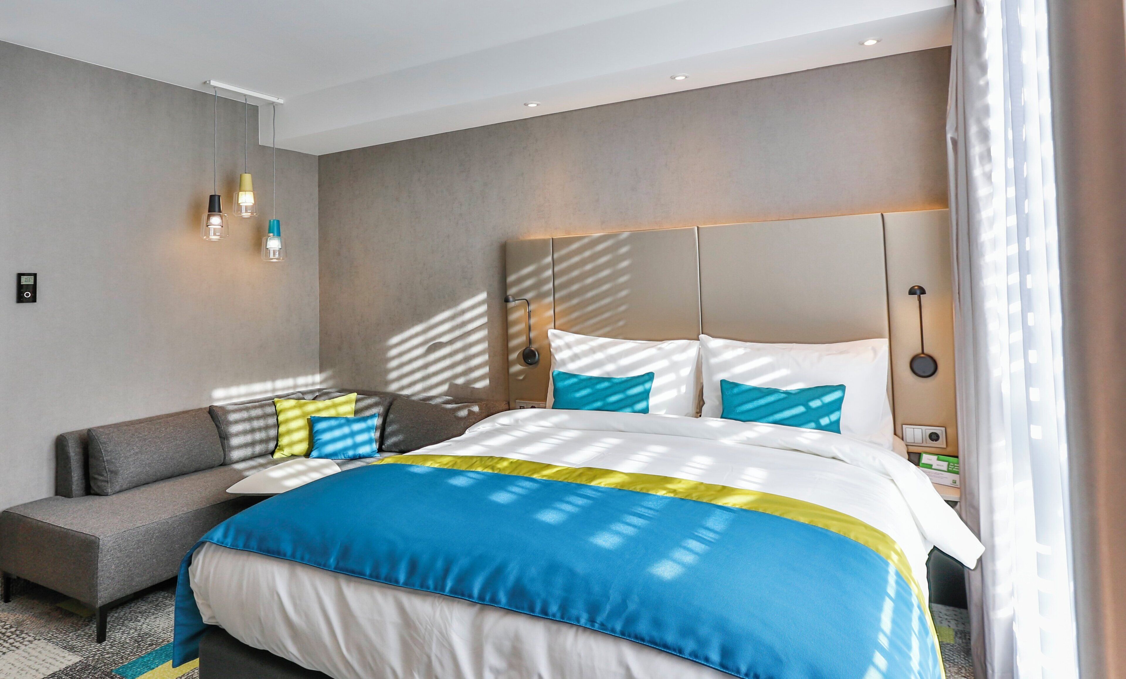 Una habitación de hotel moderna con una cama grande, un sofá y una mesita de noche con lámpara.
