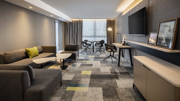 A modern hotel room with a sofa, a small table, a desk, and a TV mounted on the wall. - Holiday Inn Villingen - Schwenningen by IHG (Villingen-Schwenningen)