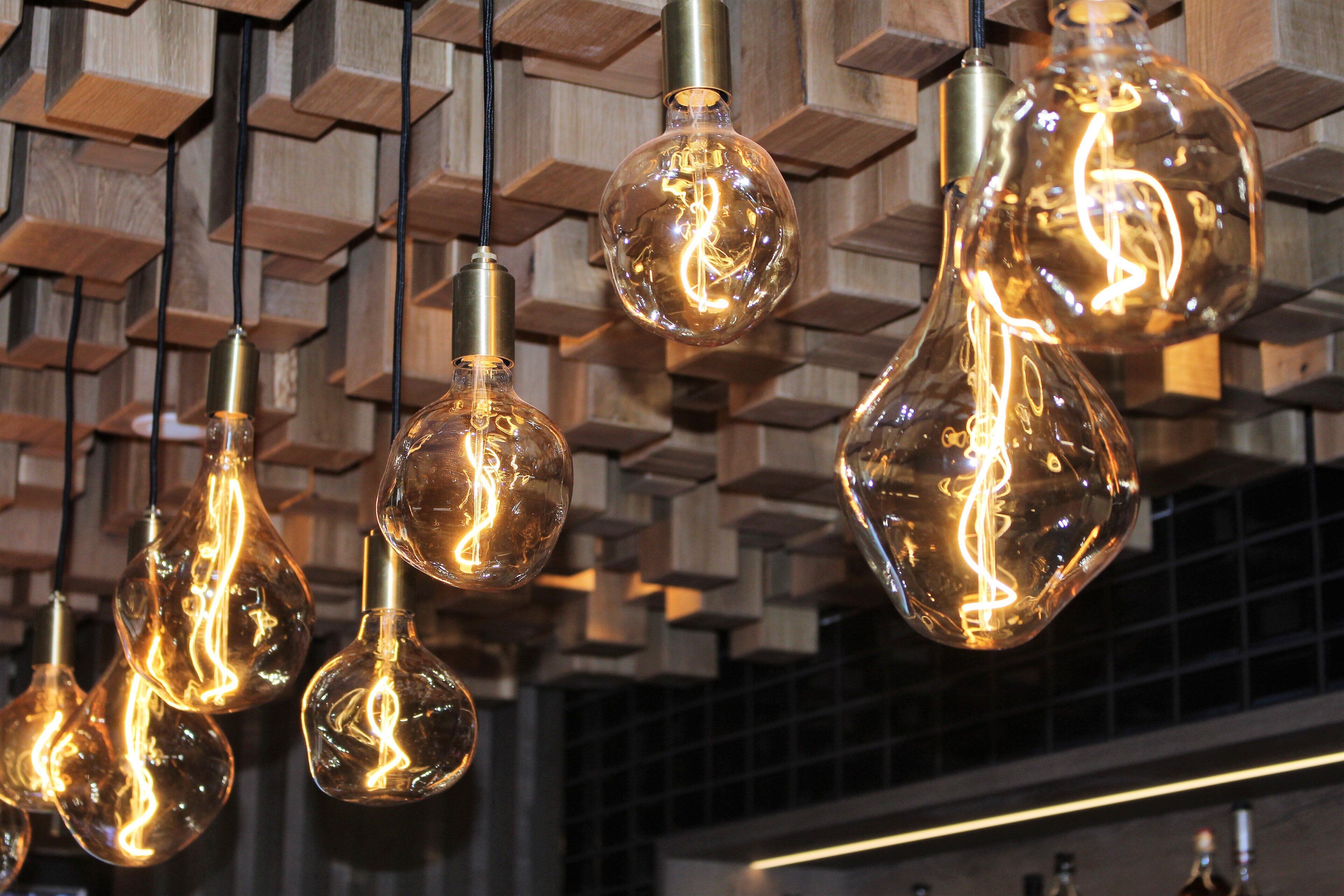 Multiple hanging light bulbs with a clear filament design, suspended from a wooden structure.