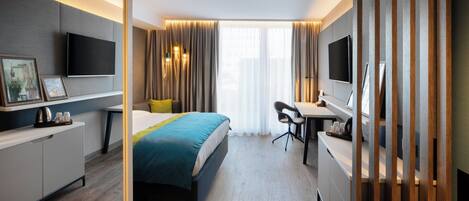 A modern hotel room with a bed, desk, and TV.