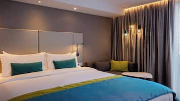 Une chambre d’hôtel moderne avec un grand lit, une table de chevet et une vue sur la ville, visible à travers les rideaux.